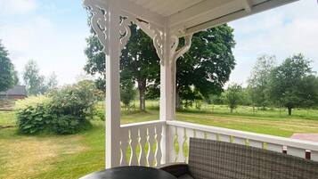 A covered outdoor seating area with a table and a bench, overlooking a grassy landscape with trees.