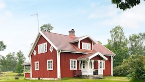 A red two-story house with a porch, a chimney, and a large lawn. - 8 Person Holiday Home in Virestad (Virestad)