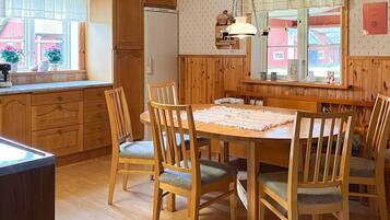 A wooden interior with a dining table surrounded by chairs, a refrigerator, and a window with a view of buildings.