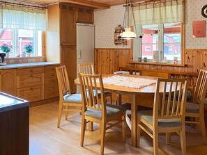 Interior de madera con una mesa de comedor rodeada de sillas, un refrigerador y una ventana con vistas a edificios.