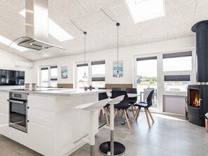 A modern kitchen with a central island, a dining area with chairs, and a wood-burning stove.