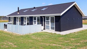 Une maison de plage moderne dotée d’un patio couvert, de grandes fenêtres et d’un toit en pente.