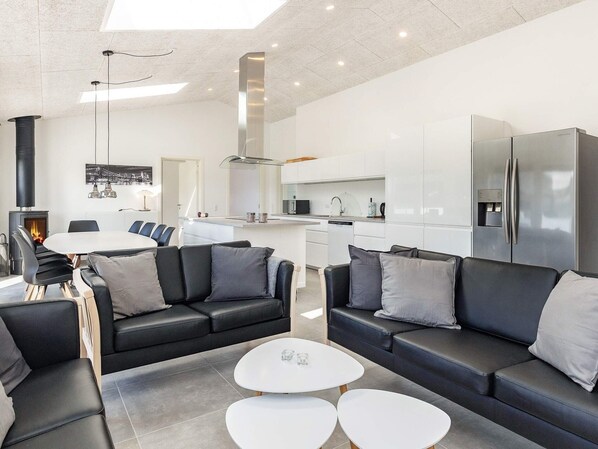Una sala de estar moderna con sofás de cuero negro, una mesa de comedor blanca y una cocina con gabinetes blancos y electrodomésticos de acero inoxidable.