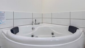 Une baignoire blanche, dotée de deux robinets et d’une molette de réglage, est placée devant un mur carrelé sur lequel est affiché un panneau.