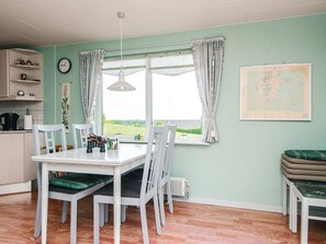 A dining area with a table and chairs, a window with curtains, a radiator, and a map on the wall. - 6 Person Holiday Home in Ebeltoft (Ebeltoft)