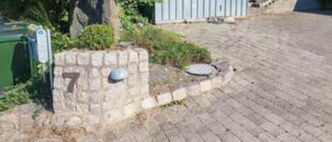 A paved driveway leading to a stone wall with a mailbox and a number plate.