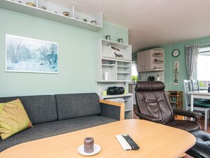 Un salon avec un canapé gris, une table basse en bois, un fauteuil en cuir marron et une bibliothèque.