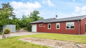 A red single-story building with a garage, a satellite dish, and a paved driveway. - 6 Person Holiday Home in Ebeltoft (Ebeltoft)