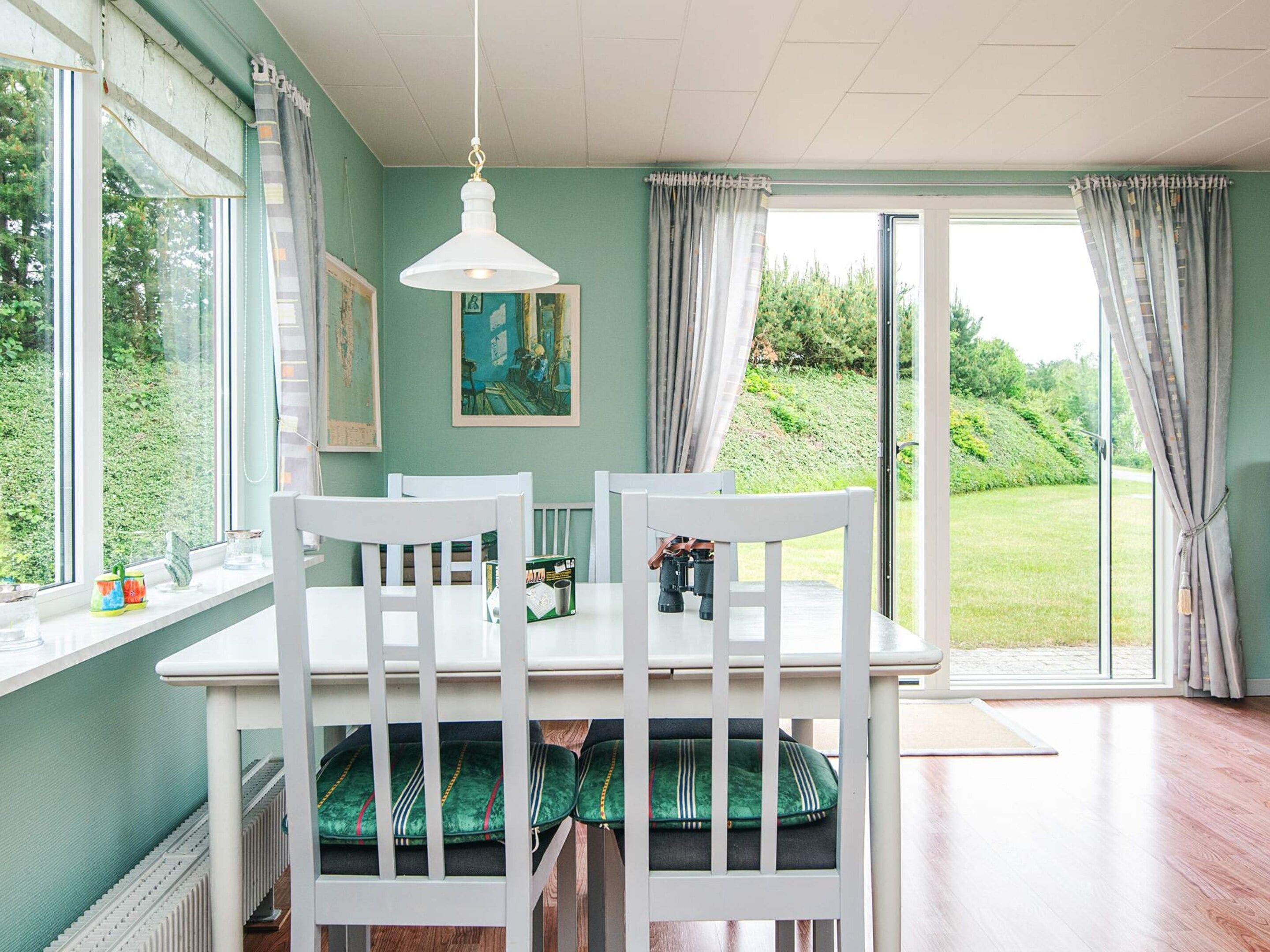 A dining area with a table, chairs, and a view of a garden through large windows.