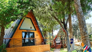 A wooden cabin with a triangular roof, surrounded by trees and a hammock. - Pamukkale Apollon Garden (Denizli)