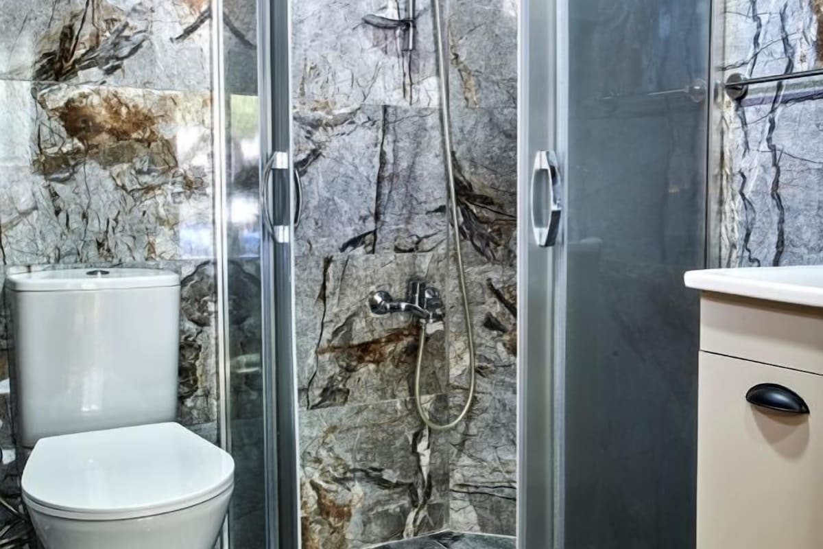 A bathroom with a glass shower enclosure, a white toilet, and a beige cabinet.