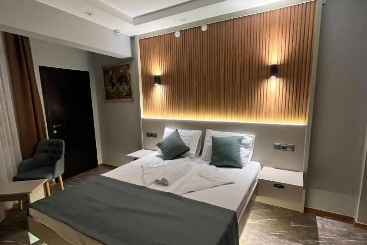 Un dormitorio moderno con una cama grande, mesitas de noche, una silla y un cabecero de madera con iluminación.