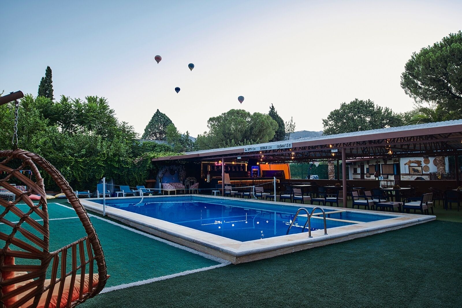 A swimming pool with a bar and seating area, surrounded by greenery and trees.
