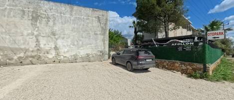 A gravel driveway, a parked SUV, a concrete wall, and a sign for 'A POLLON Garden' with an arrow pointing left to 'OTOPARK'.