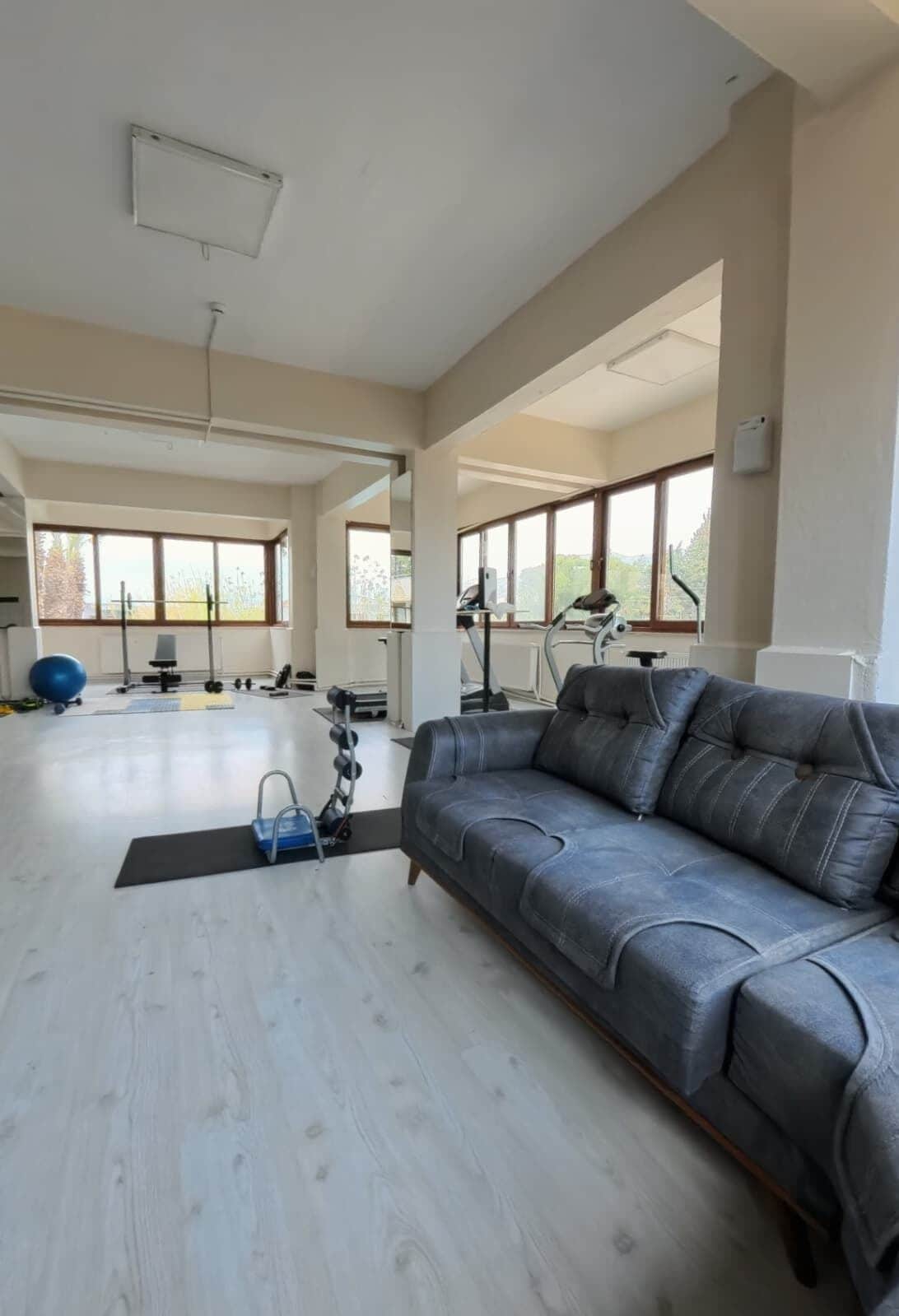 A spacious room with a grey leather sofa, a black exercise mat, and a blue exercise ball.