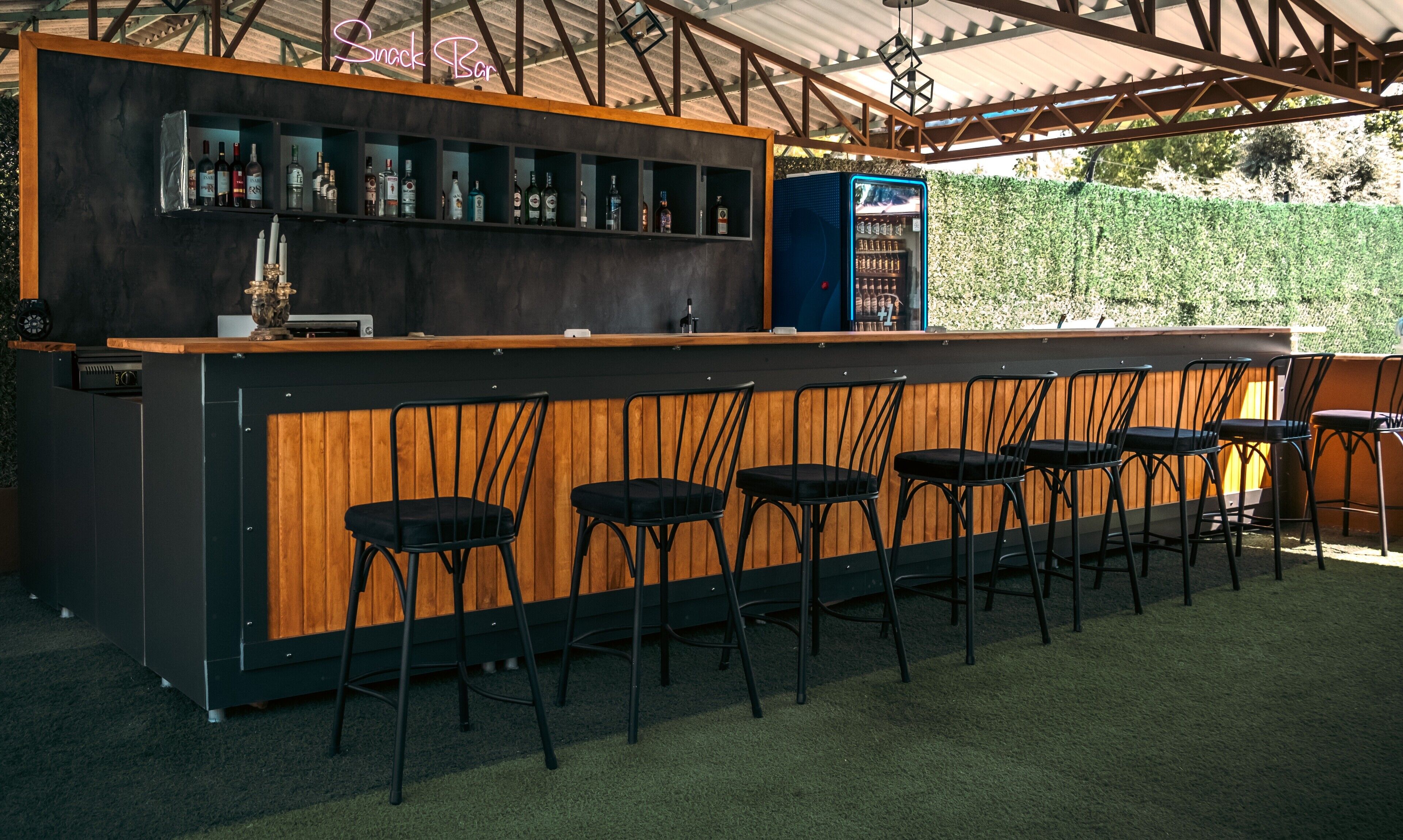 Una zona de bar con mostrador de madera, taburetes negros y un letrero de neón que dice 'Snack Bar'.