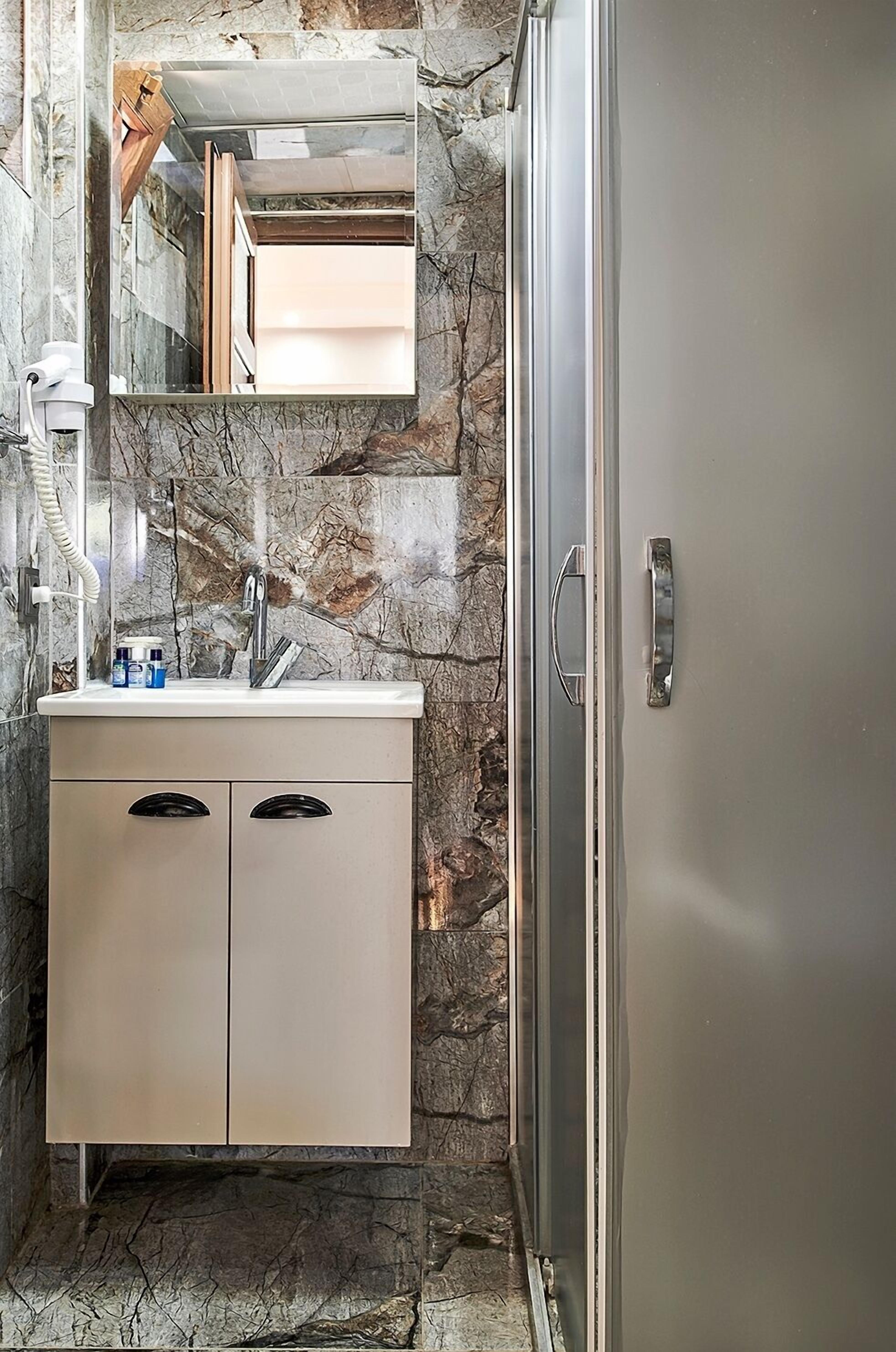 A bathroom with a marble wall, a sink with a mirror, and a cabinet.