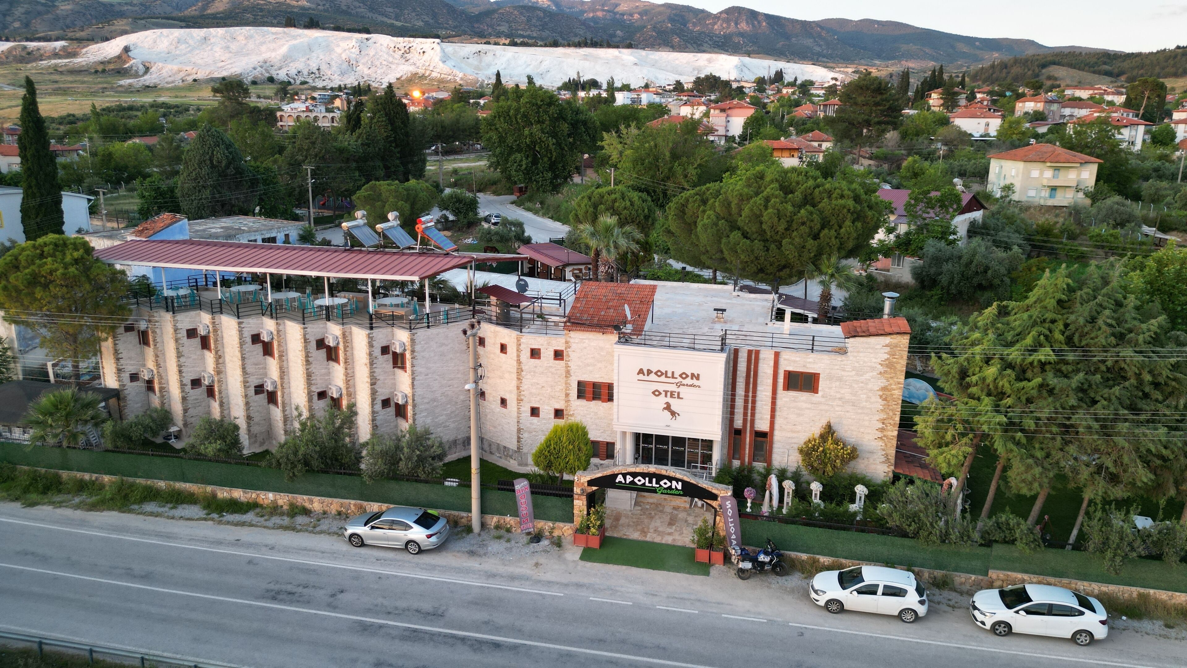 Um hotel com fachada de pedra, chamado "APOLLON Garden Hotel", com um terraço no telhado e área de estar ao ar livre.