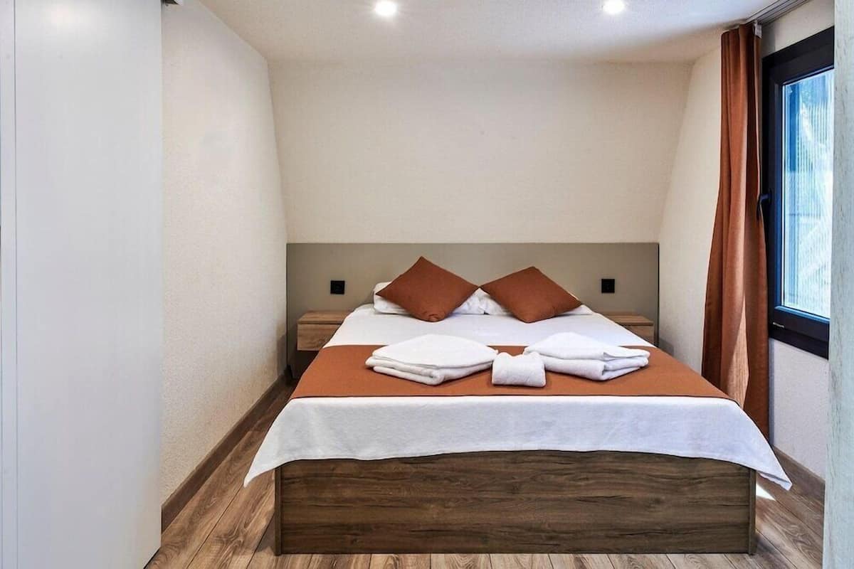 Un lit simple avec une tête de lit en bois, une literie blanche et deux oreillers marron.