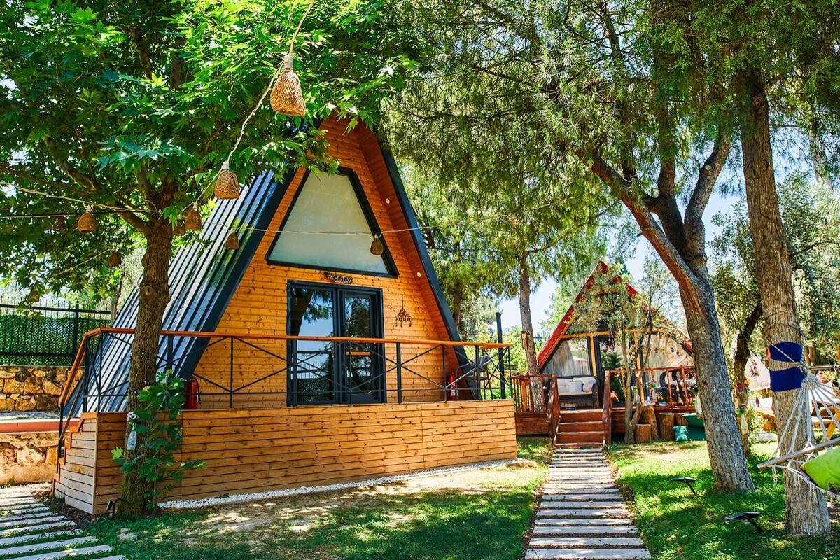 Una cabaña de madera con techo inclinado, una ventana y una escalera que lleva a una terraza.