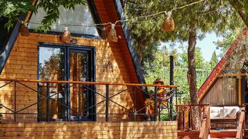 Una cabaña de madera con techo inclinado, un balcón con barandilla de metal y una escalera que lleva a una terraza.