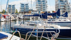 A marina with multiple boats docked, surrounded by modern buildings with balconies. - 5 Star Holiday Home in Wendtorf (Wendtorf)