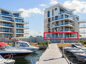 A modern multi-story building with balconies, a dock with boats, and a clear sky. - 5 Star Holiday Home in Wendtorf (Wendtorf)