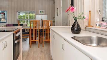 A modern kitchen with a dining area, wooden chairs, a vase with flowers, and a window with a view.