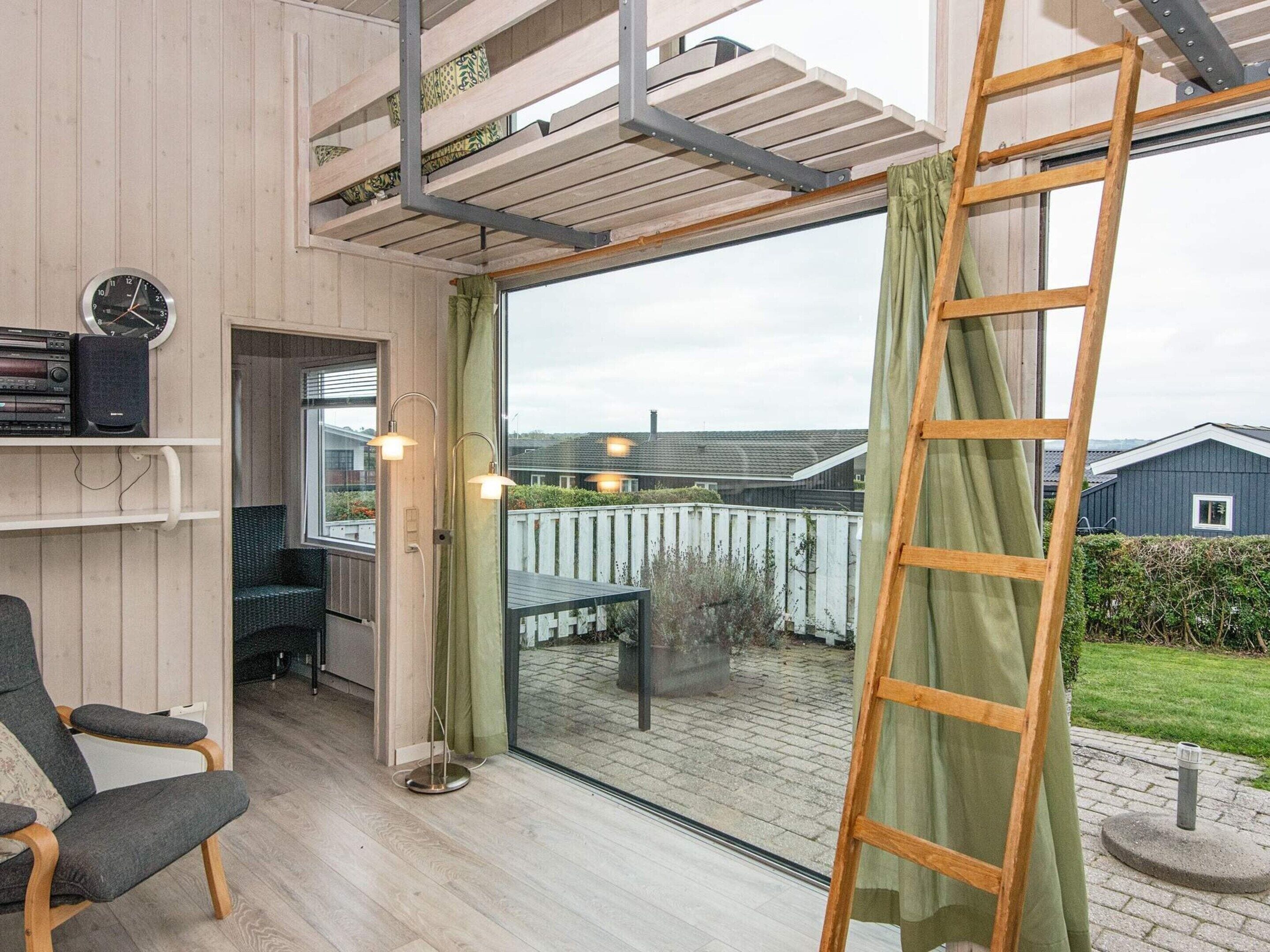 A room with a wooden floor, a chair, a table, a ladder, and a window with a view of a house and garden.