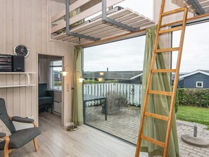 A room with a wooden floor, a chair, a table, a ladder, and a window with a view of a house and garden. - 4 Person Holiday Home in Ronde (Ronde)