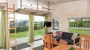 Un saló modern amb un sofà, una taula de centre, i cadires, una escala, i una finestra gran amb vistes a un jardí i cases.