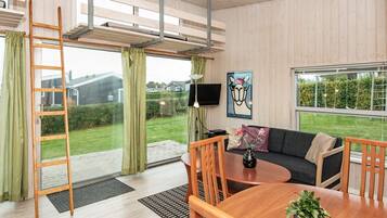 Una sala moderna con sofá, mesa de centro y sillas, una escalera y un ventanal con vistas a un jardín y casas.