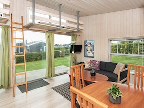 A modern living room with a sofa, coffee table, and chairs, a ladder, and a large window with a view of a garden and houses. - 4 Person Holiday Home in Ronde (Ronde)