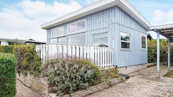 A modern blue house with a white porch, surrounded by a brick pathway and greenery.