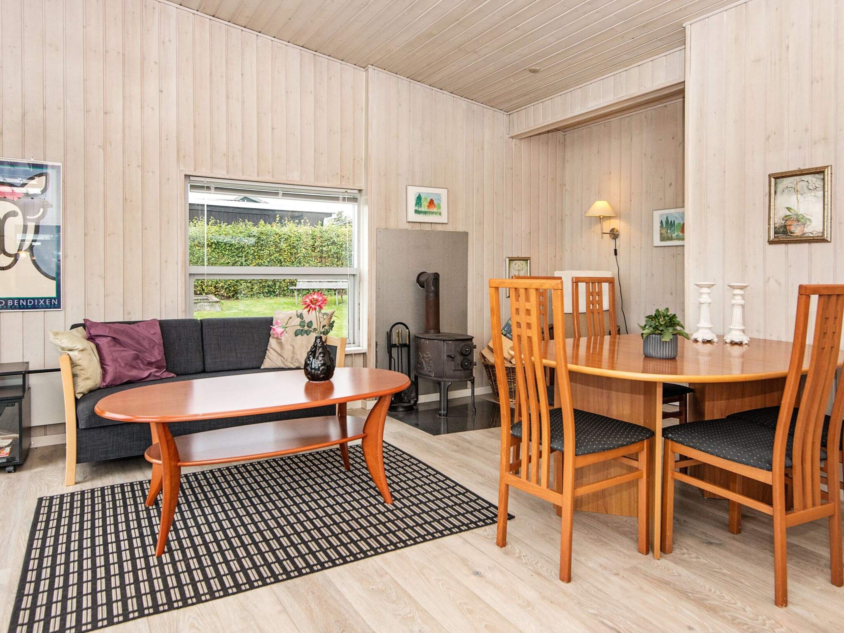 A room with a sofa, a dining table with chairs, a patterned rug, and a window with a view of greenery.