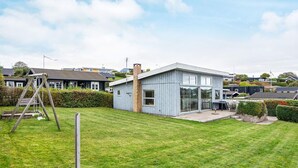 Una casa moderna amb una gran finestra de vidre, una xemeneia de maó i un jardí amb gespa.