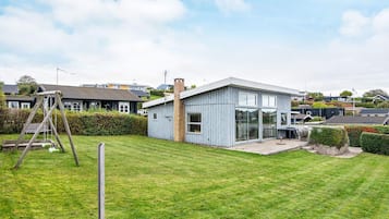 Una casa moderna con un amplio ventanal, una chimenea de ladrillo y un jardín cubierto de césped.