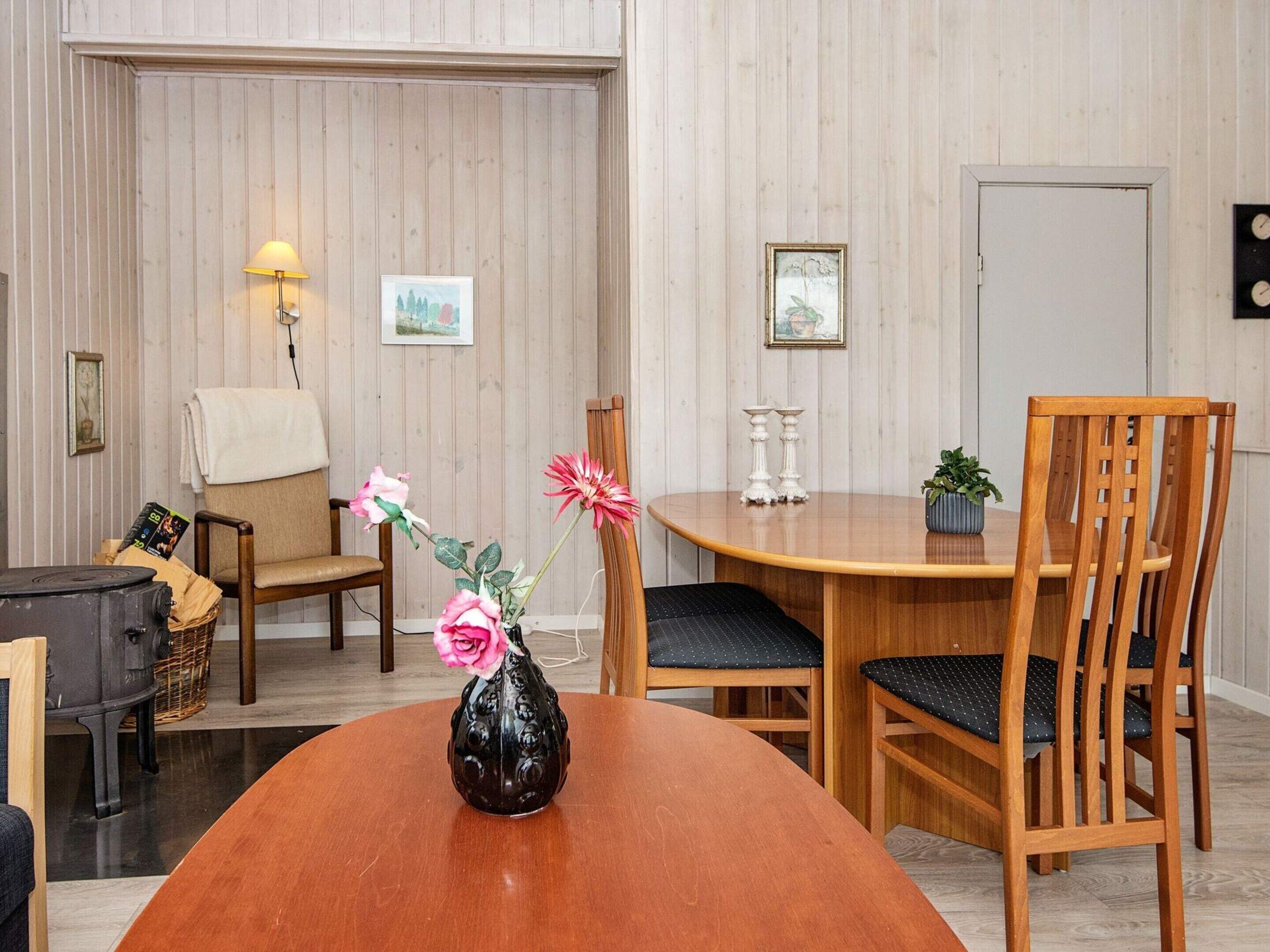 Un coin repas comprenant une table en bois, deux chaises, un vase avec des fleurs et des éléments de décoration fixés au mur.