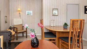 A dining area with a wooden table, two chairs, a vase with flowers, and wall-mounted decor.