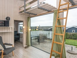 Una habitación con piso de madera, una silla, una mesa, una escalera y vistas al exterior.