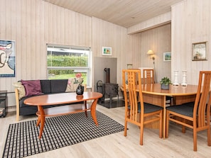 A cozy room with a sofa, a dining table with chairs, a fireplace, and a window with a view of greenery. - 4 Person Holiday Home in Ronde (Ronde)