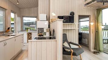 Une cuisine compacte avec un coin repas, un lambris en bois, une machine à café et une horloge au mur.