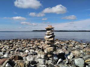 A stack of stones on a rocky shore with a calm body of water and a distant landmass in the background.