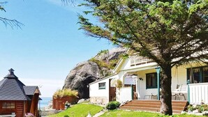 A coastal house with a stone staircase leading to a porch, surrounded by lush greenery and a large rock formation. - 4 Star Holiday Home in Skudeneshavn (Karmoy)