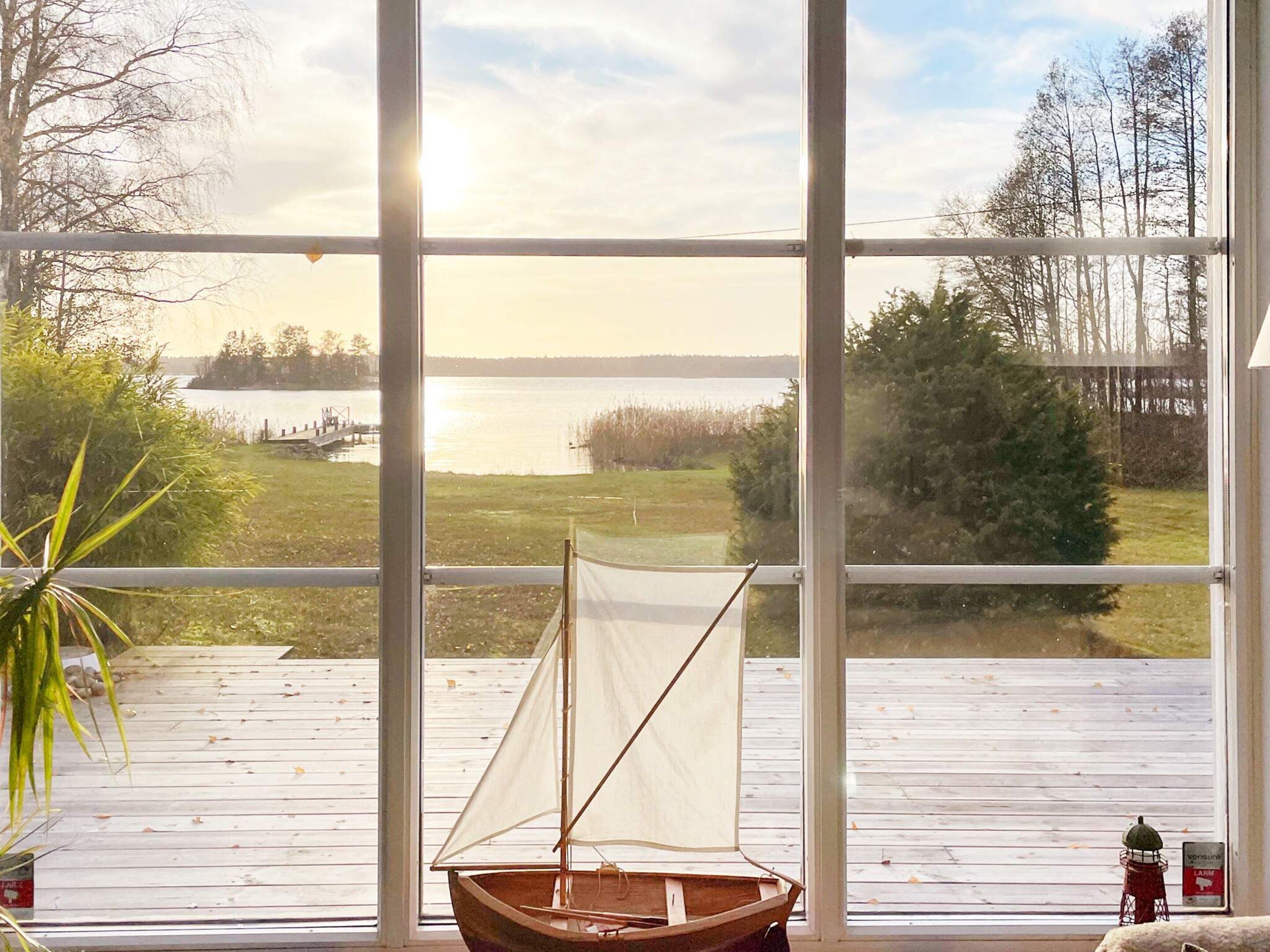A sailboat on a wooden deck with a view of a lake and trees through large windows.