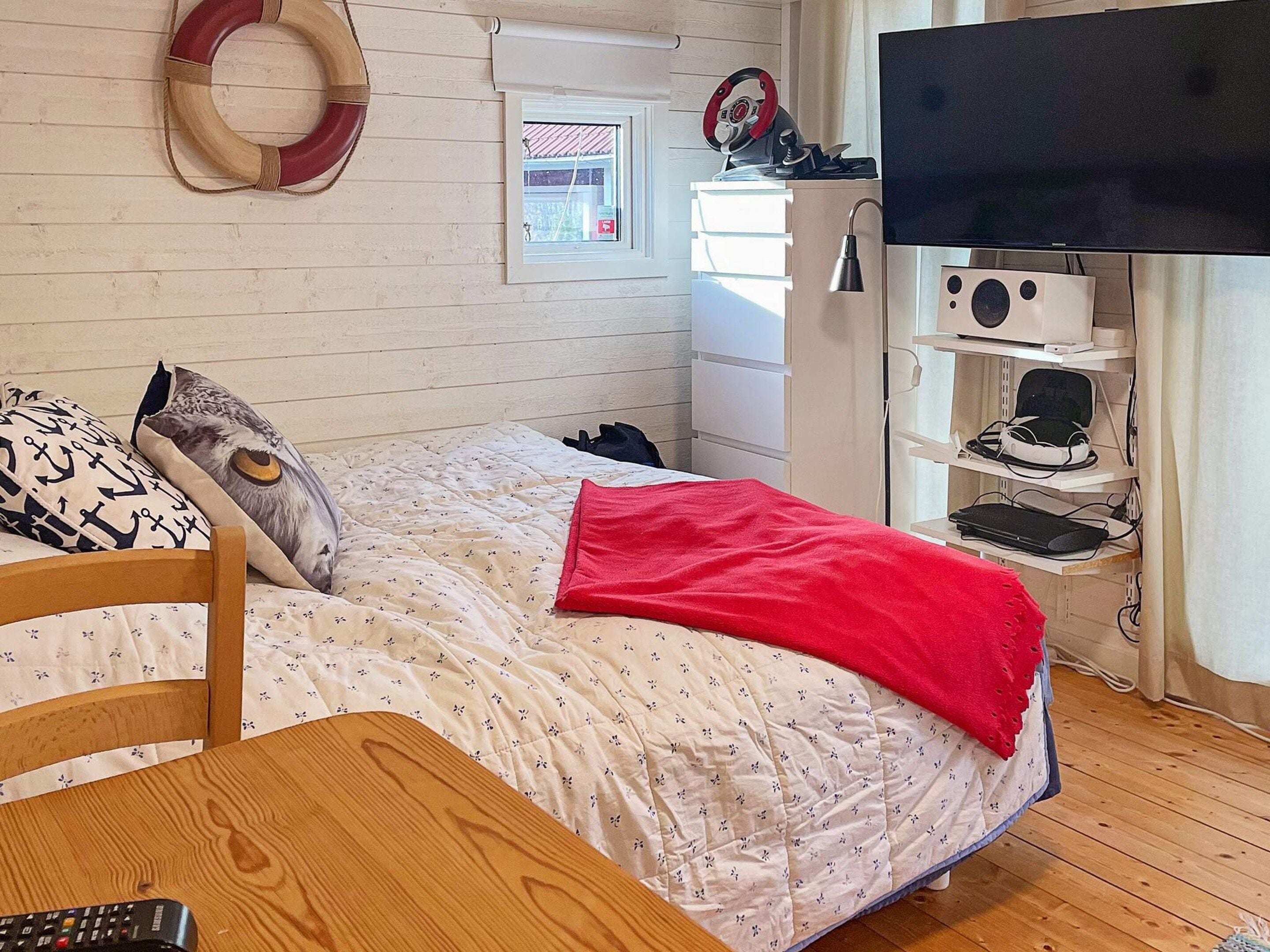 A bedroom with a bed, a desk, a TV, and a shelf with electronic devices.
