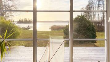 A room with a large window overlooking a lake, a small sailboat model, and a wooden deck.