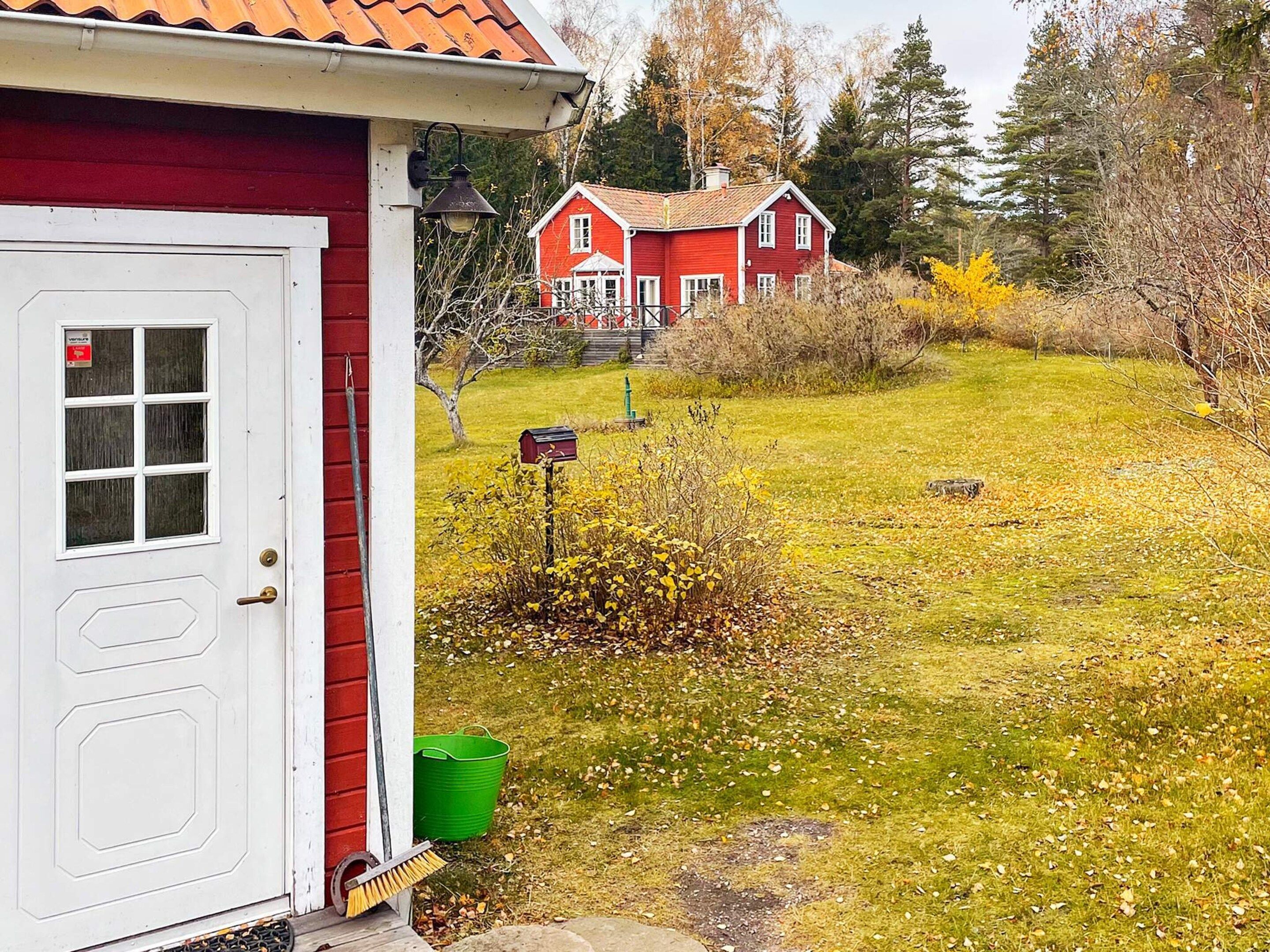 A red house with a white door, a mailbox, and a green bucket outside.