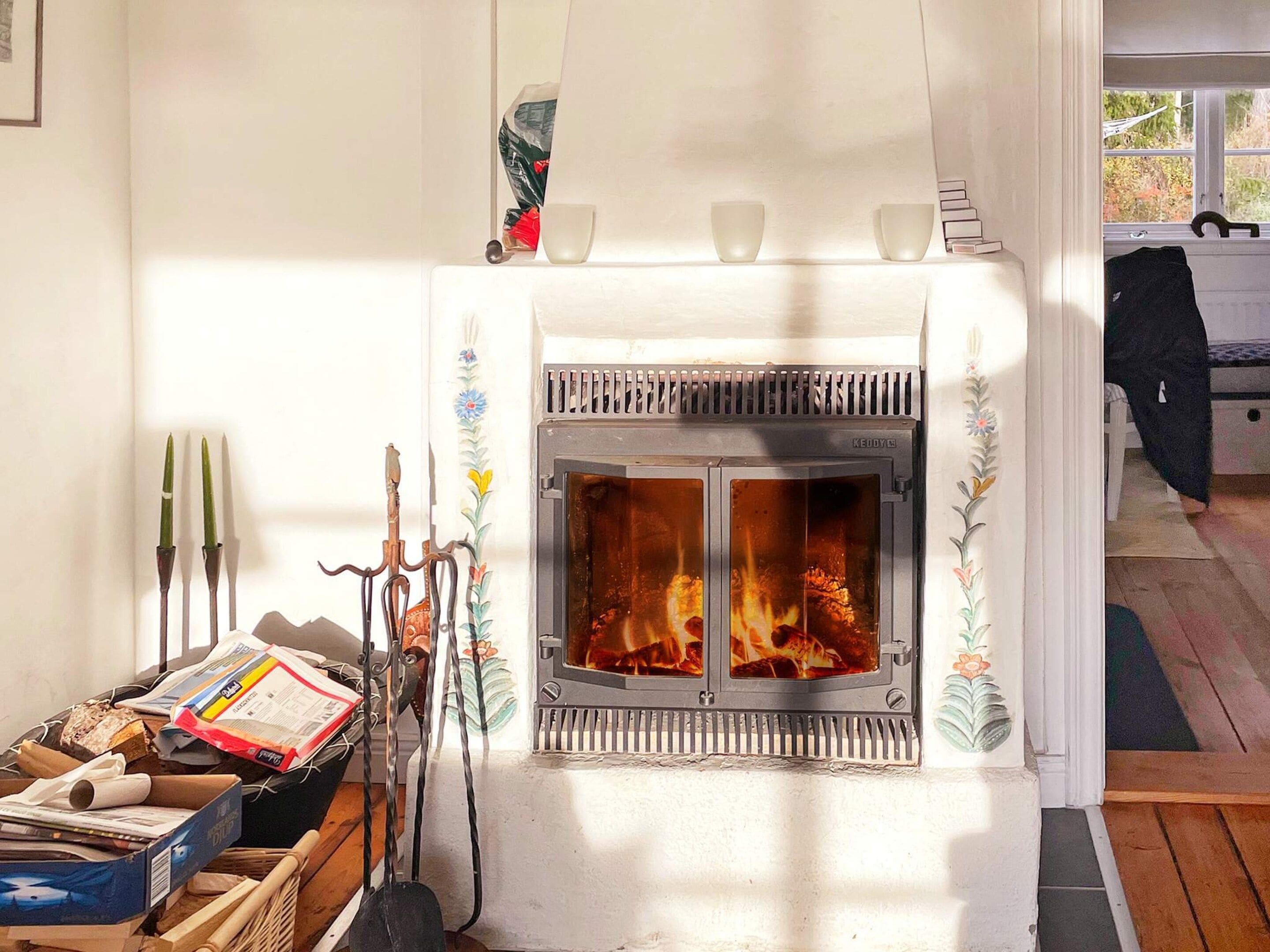 A fireplace with a white mantel and decorative elements, a wooden floor, and a window with a view of trees.