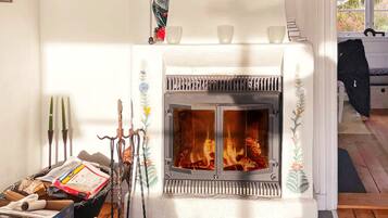 A fireplace with a white mantel and decorative elements, a wooden floor, and a window with a view of trees.